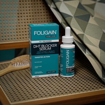 Örgülü sandalye oturağında FOLIGAIN DHT engelleyici serum şişesi ve kutusu.
