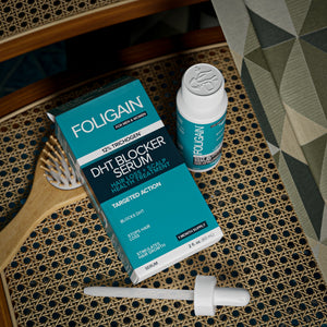 Bir saç fırçasının yanındaki FOLIGAIN DHT serum kutusu, şişesi ve damlalığının üstten görünümü.