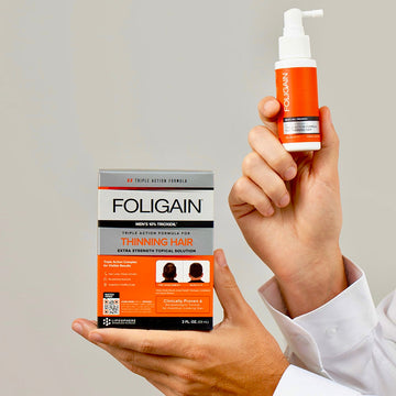 Erkekler için FOLIGAIN %10 TRIOXIDIL topikal bakım ürünü kutusunu ve sprey şişesini tutan eller.