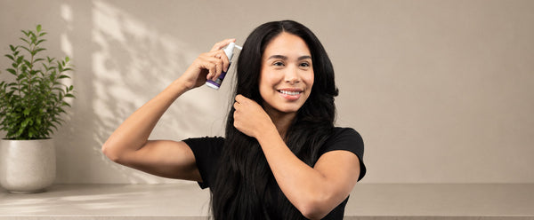 Saçını ayırıp FOLIGAIN TRIOXIDIL sprey aplikatörünü saç derisine yakın tutan kadın.
